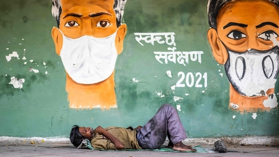 A man rests on a footpath under a Covid-19 coronavirus awareness painting in New Delhi on May 11, 2021.(AFP) A man rests on a footpath under a Covid-19 coronavirus awareness painting in New Delhi on May 11, 2021.(AFP)