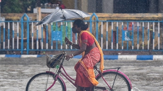 A woman holds her umbrella and wades her bicycle through a water logged road, after heavy rain in Kolkata, Tuesday, May 11, 2021. (PTI)