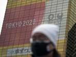 A man wearing a protective mask to help curb the spread of the coronavirus walks near a banner of the Tokyo 2020 Olympics and Paralympics.