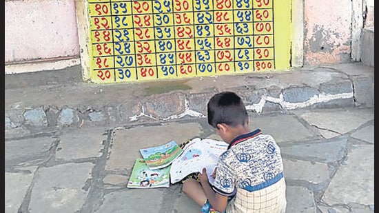 A school-going student in Mhalwadi village notes down multiplication tables painted on the wall of a shop. (HT) A school-going student in Mhalwadi village notes down multiplication tables painted on the wall of a shop. (HT)