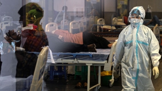 A health worker wearing a protective gear walks past Covid-19 coronavirus patients.(AFP) A health worker wearing a protective gear walks past Covid-19 coronavirus patients.