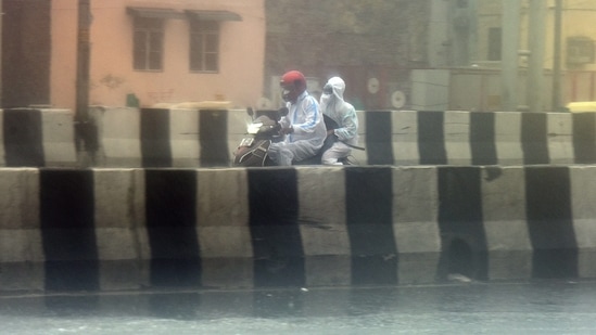 Commuters wearing PPE coveralls  out during a heavy rain spell on NH-24 road, near Akshardham Temple in New Delhi on May 19. The India Meteorological Department (IMD) said the rains were caused across much of north India under the residual impact of Cyclone Tauktae. (Raj K Raj / HT Photo)