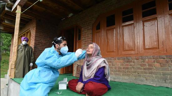 A health worker takes a nasal swab sample of a woman to test for Covid-19 outside her home at Khag in central Kashmir's Budgam district. (HT file)