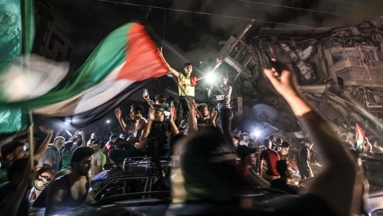 People wave the Palestinian flag as they celebrate in front of a destroyed building in Gaza City early on May 21, following the ceasefire. Palestinians who had spent 11 days huddled in fear of Israeli shelling poured into Gaza's streets, embracing one another in celebration in front of bombed-out buildings on streets covered in wreckage.(Mahmud Hams / AFP)