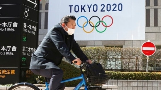 A man wearing a face mask cycles past the logo of the Tokyo Olympics. (AP) A man wearing a face mask cycles past the logo of the Tokyo Olympics. (AP)