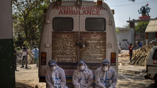 Exhausted workers, who bring dead bodies for cremation, sit on the rear step of an ambulance inside a crematorium, in New Delhi.