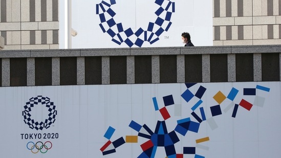 A man wearing a face mask walks by the logo of the Tokyo Olympics, in Tokyo, (AP)