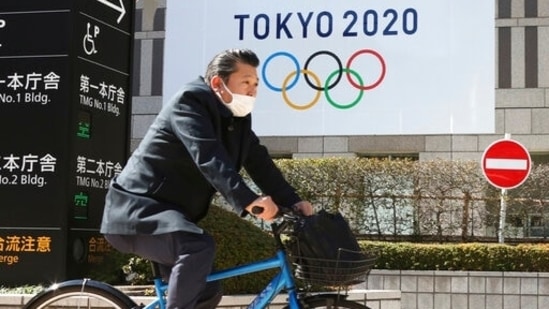 A man wearing a face mask cycles past the logo of the Tokyo Olympics, in Tokyo.(AP) A man wearing a face mask cycles past the logo of the Tokyo Olympics, in Tokyo.(AP)