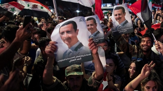 Syrian President Bashar Assad supporters hold up national flags and pictures of Assad as they celebrate at Omayyad Square, in Damascus.(AP)