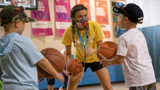 A counselor wearing a protective face mask plays with children as summer camps reopen amid the spread of coronavirus disease (Covid-19). (REUTERS)