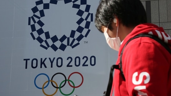 A man walks by the logo of the Tokyo Olympics, in Tokyo,(AP)