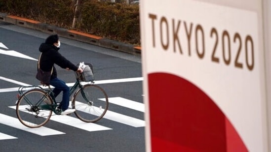 FILE - In this Jan. 21, 2021, file photo, a man wearing a protective mask to help curb the spread of the coronavirus rides a bicycle near a banner of the Tokyo 2020 Olympics. (AP) FILE - In this Jan. 21, 2021, file photo, a man wearing a protective mask to help curb the spread of the coronavirus rides a bicycle near a banner of the Tokyo 2020 Olympics. (AP)