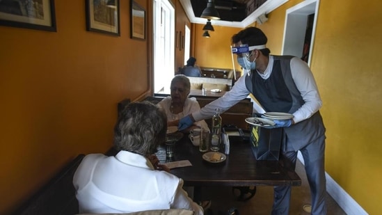 A waiter wearing a face mask, gloves and shield serves diners at Town Hall restaurant as lockdown restrictions ease, in Khan Market. (Biplov Bhuyan/ Hindustan Times)