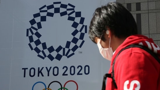 A man walks by the logo of the Tokyo Olympics, in Tokyo, (AP) A man walks by the logo of the Tokyo Olympics, in Tokyo, (AP)