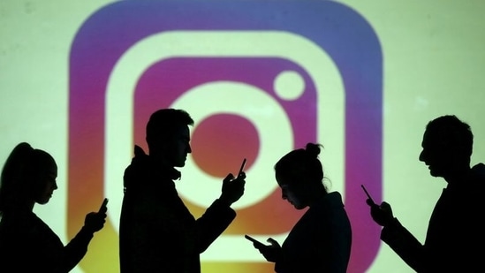 Silhouettes of mobile users are seen next to a screen projection of Instagram logo in this picture illustration.(REUTERS)