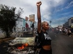 A protester raises her fist in the air next to a burning police vehicle in Los Angeles during a demonstration over the death of George Floyd. (AP) A protester raises her fist in the air next to a burning police vehicle in Los Angeles during a demonstration over the death of George Floyd. (AP)