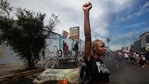 A protester raises her fist in the air next to a burning police vehicle in Los Angeles during a demonstration over the death of George Floyd. (AP) A protester raises her fist in the air next to a burning police vehicle in Los Angeles during a demonstration over the death of George Floyd. (AP)