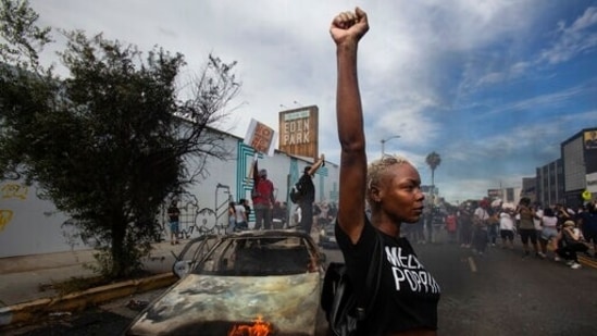 A protester raises her fist in the air next to a burning police vehicle in Los Angeles during a demonstration over the death of George Floyd. (AP)