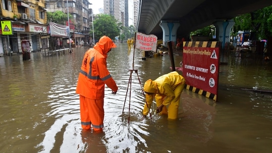 Municipal workers standing near an open manhole to divert people, on a waterlogged road in Parel, Mumbai on June 9. Mayor Kishori Pednekar on June 10 said that 458 pumps have been installed to pump out the rainwater and work is underway to cover 73000 manholes in the city.(Bhushan Koyande / HT Photo)