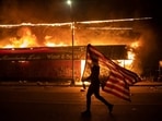 A protester carries a US flag upside down, a sign of distress, next to a burning building, May 28, 2020, in Minneapolis. (Julio Cortez / AP Photo)