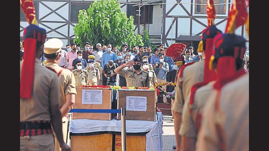 A police officer paying tribute to the slain cops as locals mourn in the backdrop during a wreath laying ceremony in Srinagar on Saturday. (Waseem Andrabi/HT)