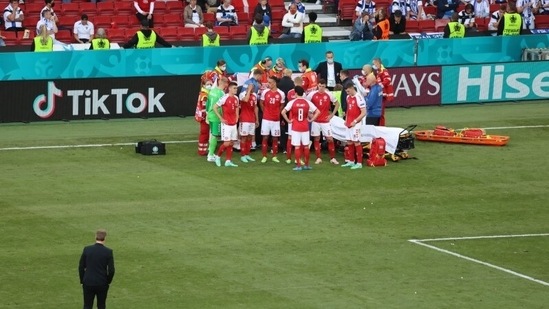 Denmark coach Kasper Hjulmand walks towards the Denmark players next to Christian Eriksen as he receives medical attention after collapsing during the match.