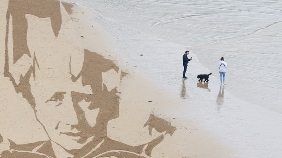 An incoming tide washes away a part of a giant beach sand artwork depicting the face of British Prime Minister Boris Johnson and other G7 leaders, created by campaign group Avaaz, at Watergate Bay Beach on June 10.(Tom Nicholson / REUTERS)