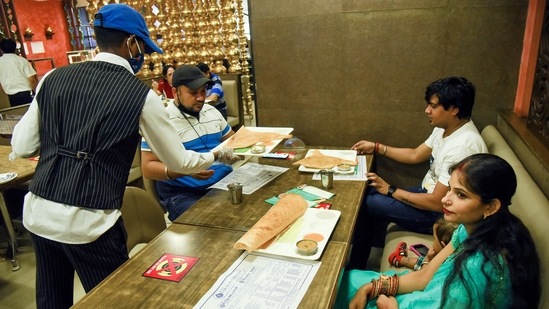 A waiter serves food to the customers at a restaurant after the state government allows the reopening of restaurants with 50% capacity, at Connaught Place in New Delhi on Monday. (ANI Photo) A waiter serves food to the customers at a restaurant after the state government allows the reopening of restaurants with 50% capacity, at Connaught Place in New Delhi on Monday. (ANI Photo)
