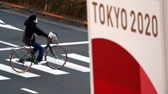 FILE - A man wearing a protective mask to help curb the spread of the coronavirus rides a bicycle near a banner of the Tokyo 2020 Olympics in Tokyo.(AP) FILE - A man wearing a protective mask to help curb the spread of the coronavirus rides a bicycle near a banner of the Tokyo 2020 Olympics in Tokyo.(AP)