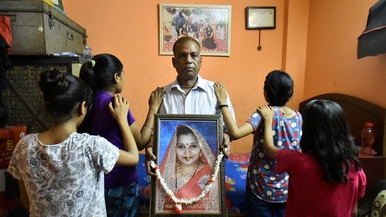 A father along with his daughters stands for a photograph while he holds a portrait of his wife, who he alleges died after developing a fever following the inoculation of Covishield, a Covid-19 vaccine, in New Delhi on May 11.(Arun Sharma / PTI)