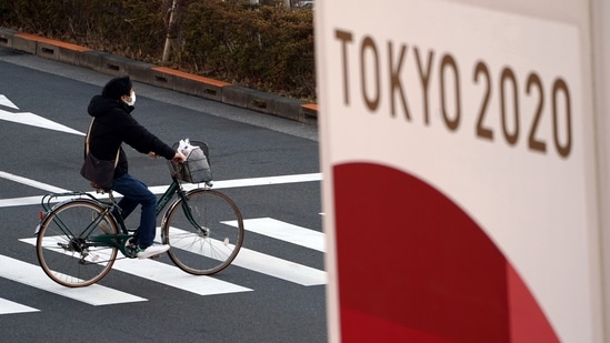 In this file photo, a man wearing a protective mask to help curb the spread of the coronavirus rides a bicycle near a banner of the Tokyo 2020 Olympics in Tokyo. (AP) In this file photo, a man wearing a protective mask to help curb the spread of the coronavirus rides a bicycle near a banner of the Tokyo 2020 Olympics in Tokyo. (AP)
