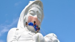 Workers place a mask on a 57-metre-high statue of Buddhist goddess Kannon to pray for the end of the coronavirus disease (COVID-19) pandemic at Houkokuji Aizu Betsuin temple in Aizuwakamatsu, Fukushima Prefecture, Japan in this handout photo taken on June 15 2021.