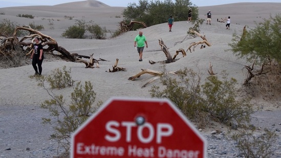Extreme heat danger signage stands as visitors walk along sand dunes at sunset inside Death Valley National Park in June 17 in Inyo County, California. The U.S National Park Service has warned of extreme summer heat, urging tourists to carry extra water and "travel prepared to survive" in the hottest, lowest, and driest national park featuring steady drought and extreme climates.(Patrick T. Fallon / AFP)
