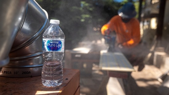 A water bottle placed nearby as a contractor uses a saw to cut siding for a house under construction in Walnut Creek, California on June 17. The triple-digit heat wave gripping the western US is also straining power supplies, risking large scale blackouts.(David Paul Morris / Bloomberg)