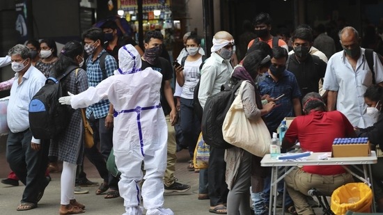 Health worker directs arriving passengers towards Covid-19 testing counter outside a train station in Bengaluru. (AP) Health worker directs arriving passengers towards Covid-19 testing counter outside a train station in Bengaluru. (AP)