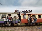 Commuters hang on the gates and sit on the roof while traveling by a crowded train. (PTI Photo) Commuters hang on the gates and sit on the roof while traveling by a crowded train. (PTI Photo)