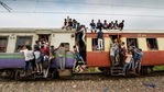 Commuters hang on the gates and sit on the roof while traveling by a crowded train. (PTI Photo) Commuters hang on the gates and sit on the roof while traveling by a crowded train. (PTI Photo)