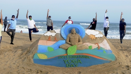 Enthusiast practice Yoga as sand artist Manas Sahoo creates a sand sculpture ahead of International Yoga Day, in Puri. (PTI)