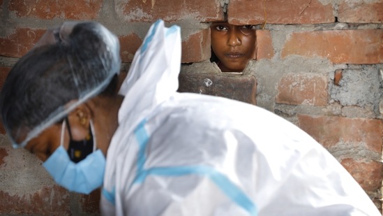 A girl looks out from a hole in the wall of her house as a health worker prepares for Covid-19 testing in Jamsoti village, Uttar Pradesh on June 9. Delivering vaccines in the world's second-most populous country was always going to be challenging. Even though India did relatively well at the beginning of its mammoth vaccination drive, the campaign hit a snag almost immediately due to shortages, exacerbating existing inequalities.(Rajesh Kumar Singh / AP)