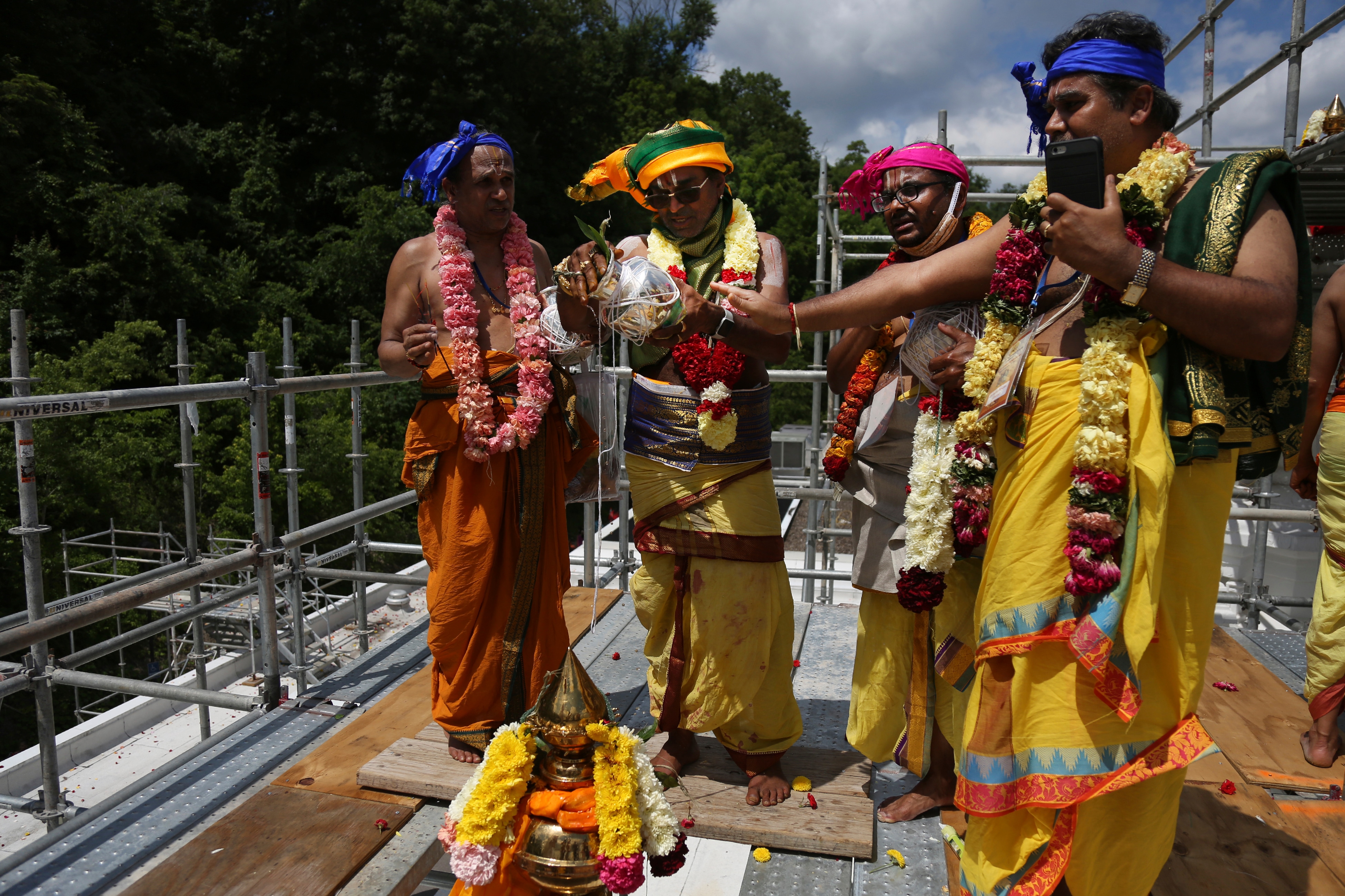 Os sacerdotes, a partir da esquerda, Sri Ranganathan, o sacerdote chefe do templo Sri Samudrala Venkatacharyulu, Sri Kannan Srinivasan e Sri Rangarajan derramam águas sagradas em uma torre conhecida como kalasham no topo do gopuram, uma torre de templo ornamentada, durante a cerimônia de rededicação hindu. (AP)