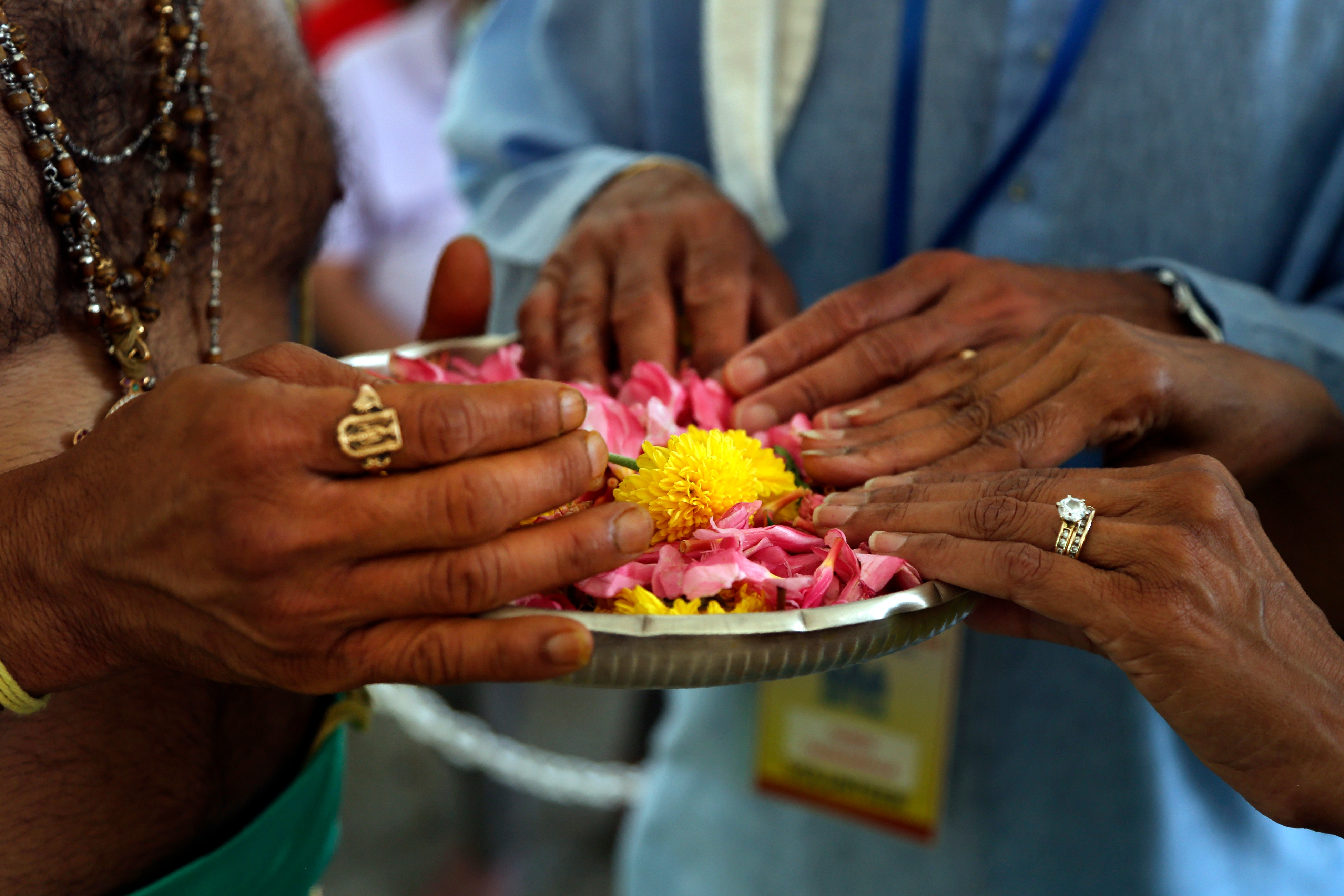 O sacerdote hindu Gopala Dhattar, à esquerda, dá bênçãos a Pandu Tadikamalla, no centro, e sua esposa, Rama Tadikamalla, à direita, enquanto eles pousam as mãos em um canteiro de pétalas de flores durante o Maha Kumbhabhishekam. (AP)