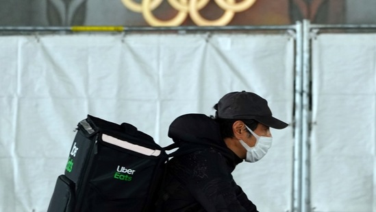 An Uber Eats delivery person carries items near the Japan National Stadium, where opening ceremony and other events are planned for postponed Tokyo 2020 Olympics, with engravings in honor of 1964 Tokyo Olympics seen on the side of the stadium wall behind the fence Tuesday, April 6, 2021, in Tokyo. Two top officials of Japan's ruling LDP party on Thursday, April 15, 2021, said radical changes could be coming to the Tokyo Olympics. One went as far to suggest they still could be canceled, and the other that even if they proceed, it might be without any fans.(AP Photo/Eugene Hoshiko) (AP) An Uber Eats delivery person carries items near the Japan National Stadium, where opening ceremony and other events are planned for postponed Tokyo 2020 Olympics, with engravings in honor of 1964 Tokyo Olympics seen on the side of the stadium wall behind the fence Tuesday, April 6, 2021, in Tokyo. Two top officials of Japan's ruling LDP party on Thursday, April 15, 2021, said radical changes could be coming to the Tokyo Olympics. One went as far to suggest they still could be canceled, and the other that even if they proceed, it might be without any fans.(AP Photo/Eugene Hoshiko) (AP)