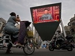 A woman on her electric-powered scooter films a large video screen outside a shopping mall showing Chinese President Xi Jinping speaking during an event to commemorate the 100th anniversary of China's Communist Party at Tiananmen Square in Beijing on July 1.