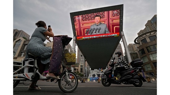 A woman on her electric-powered scooter films a large video screen outside a shopping mall showing Chinese President Xi Jinping speaking during an event to commemorate the 100th anniversary of China's Communist Party at Tiananmen Square in Beijing on July 1.(Andy Wong / AP)