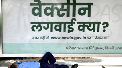 A man takes a nap under a bus stand horading which promotes Covid-19 vaccination campaign in the capital, in New Delhi on Thursday. (ANI Photo) A man takes a nap under a bus stand horading which promotes Covid-19 vaccination campaign in the capital, in New Delhi on Thursday. (ANI Photo)