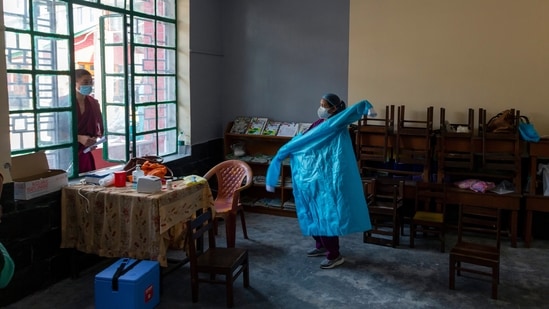 An exiled Tibetan Buddhist monk talks to a nurse as she puts on her protective suit to assist at a Covid-19 vaccination center in Dharmshala on July 1. While still elevated, the number of new infections has eased to two-month lows since hitting a peak of 400,000 a day in May.(Ashwini Bhatia / AP)