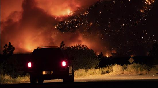 A motorist on the Trans-Canada Highway as a wildfire burns on the side of a mountain in Lytton, British Columbia. (AP)