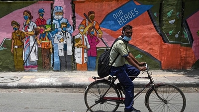 A cyclist passes by a wall mural depicting frontline Covid-19 coronavirus workers, in New Delhi. (Money Sharma / AFP)