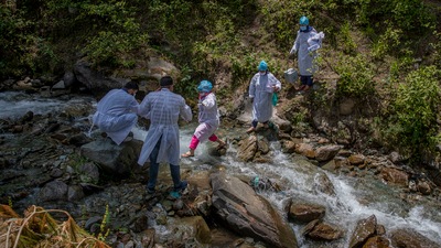 A team of health workers cross a stream to reach the villages on the upper reaches during a COVID-19 vaccination drive in Gund, northeast of Srinagar on June 22. The challenge for health workers travelling long distances to vaccinate mostly shepherds and nomadic herders in the remote meadows of the region has not been the terrain but vaccine hesitancy. (Dar Yasin / AP)