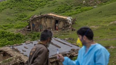 A woman watches villagers being vaccinated as she stands outside her hut during a Covid-19 vaccination drive in Tosamaidan, southwest of Srinagar on June 21. Almost 53% in Kashmir have had a first shot. (Dar Yasin / AP)